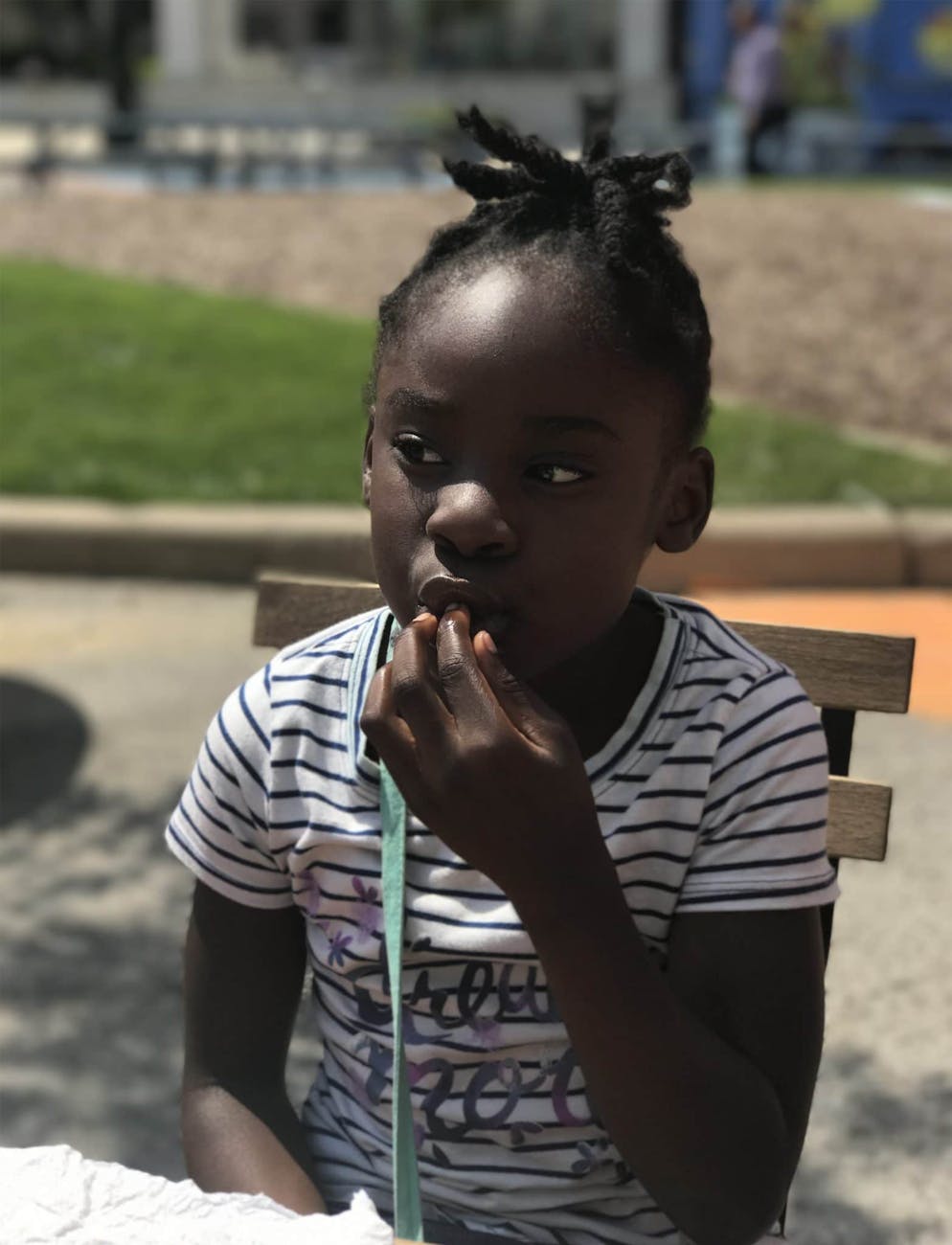 girl with her fingers in mouth while sitting on a wooden chair