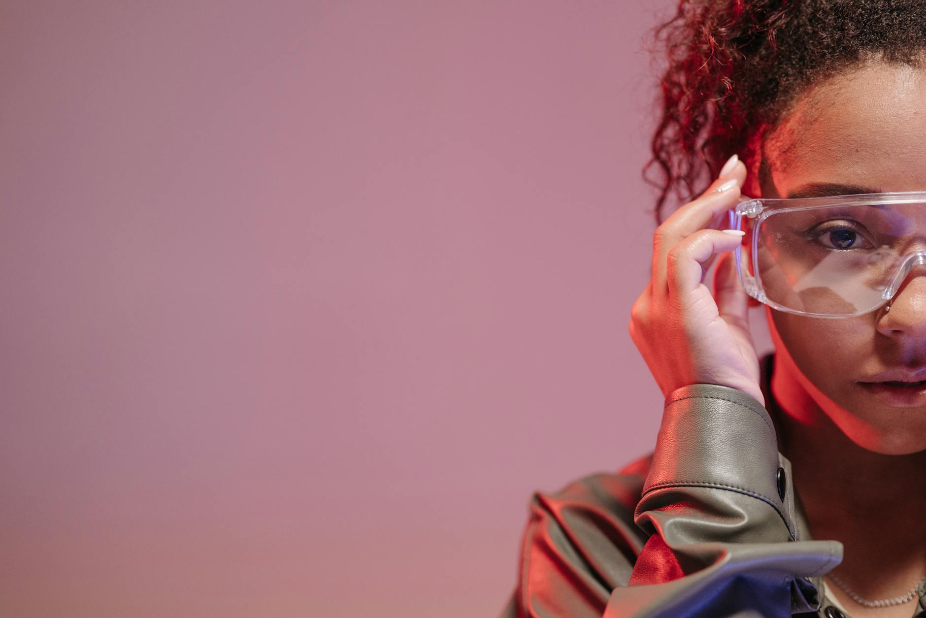close up shot of a curly haired woman wearing protective googles on pink background