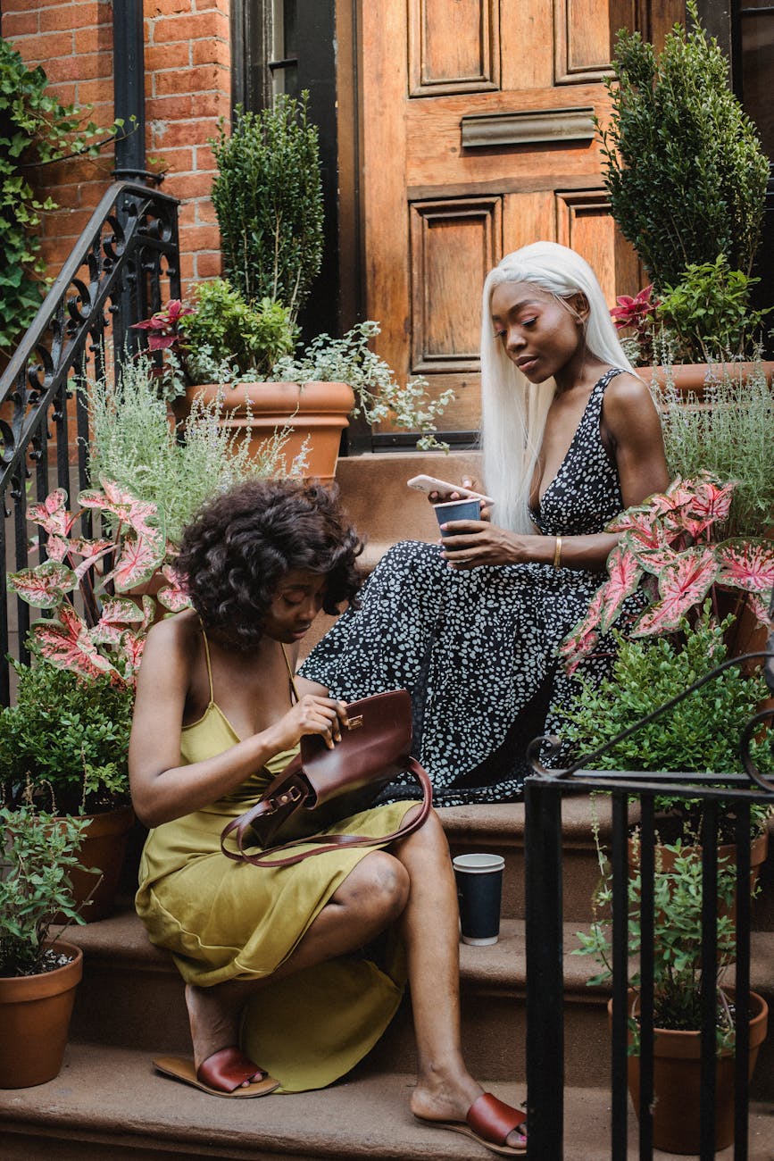 woman in floral dress with white hair sitting on stairs near a woman in olive spaghetti strap dress